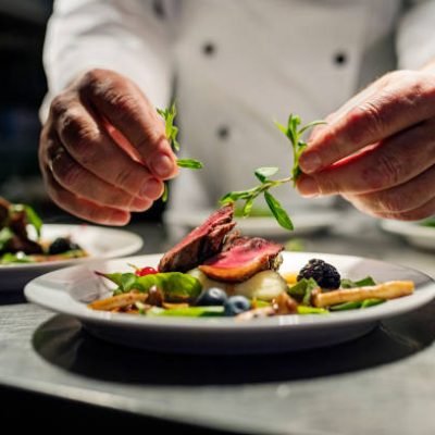 Chef adding the final flourish by adding some liquorice flavoured parsley to the dish. The dish is, pan fried pink duck breast onto a bed of parsnip puree with seasonal autumn vegetables and berries. Colour, horizontal with some copy space, photographed on location in a restaurant on the island of Møn in Denmark.